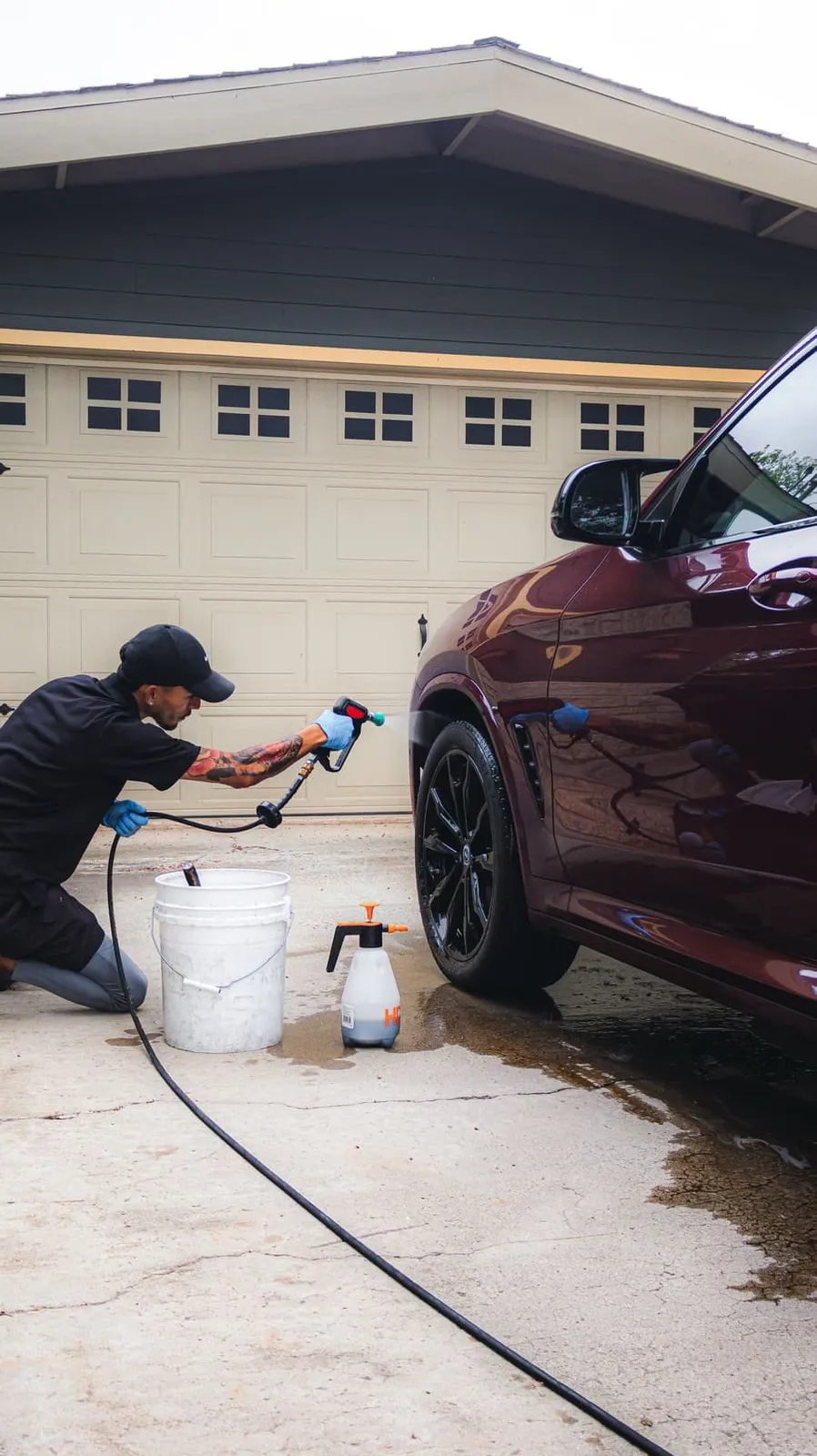 Joji's Mobile Detailing technician foam pre-washing a BMW's wheel in a San Diego driveway